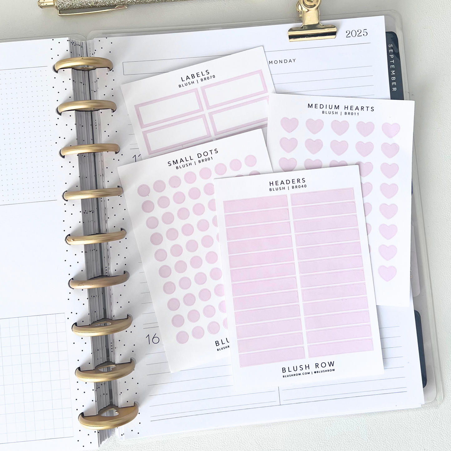 Blush header, small dot, medium heart, and label planner stickers on Blush Row sticker sheets placed on top of an open planner.